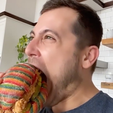 A person taking a bite out of a chicken sandwich with a bun made from Airheads Xtremes Belts.